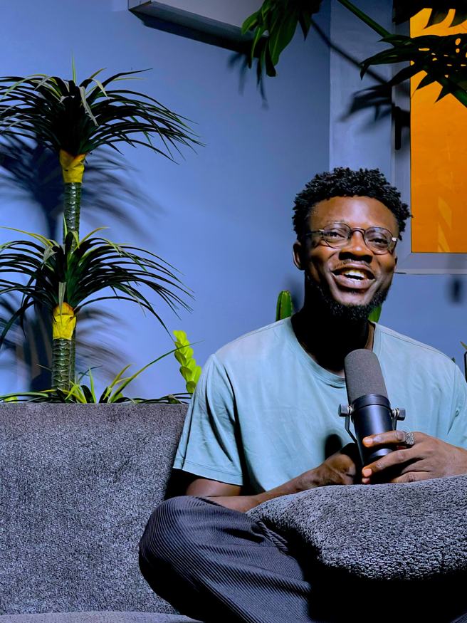 Smiling on a studio sofa with a microphone
